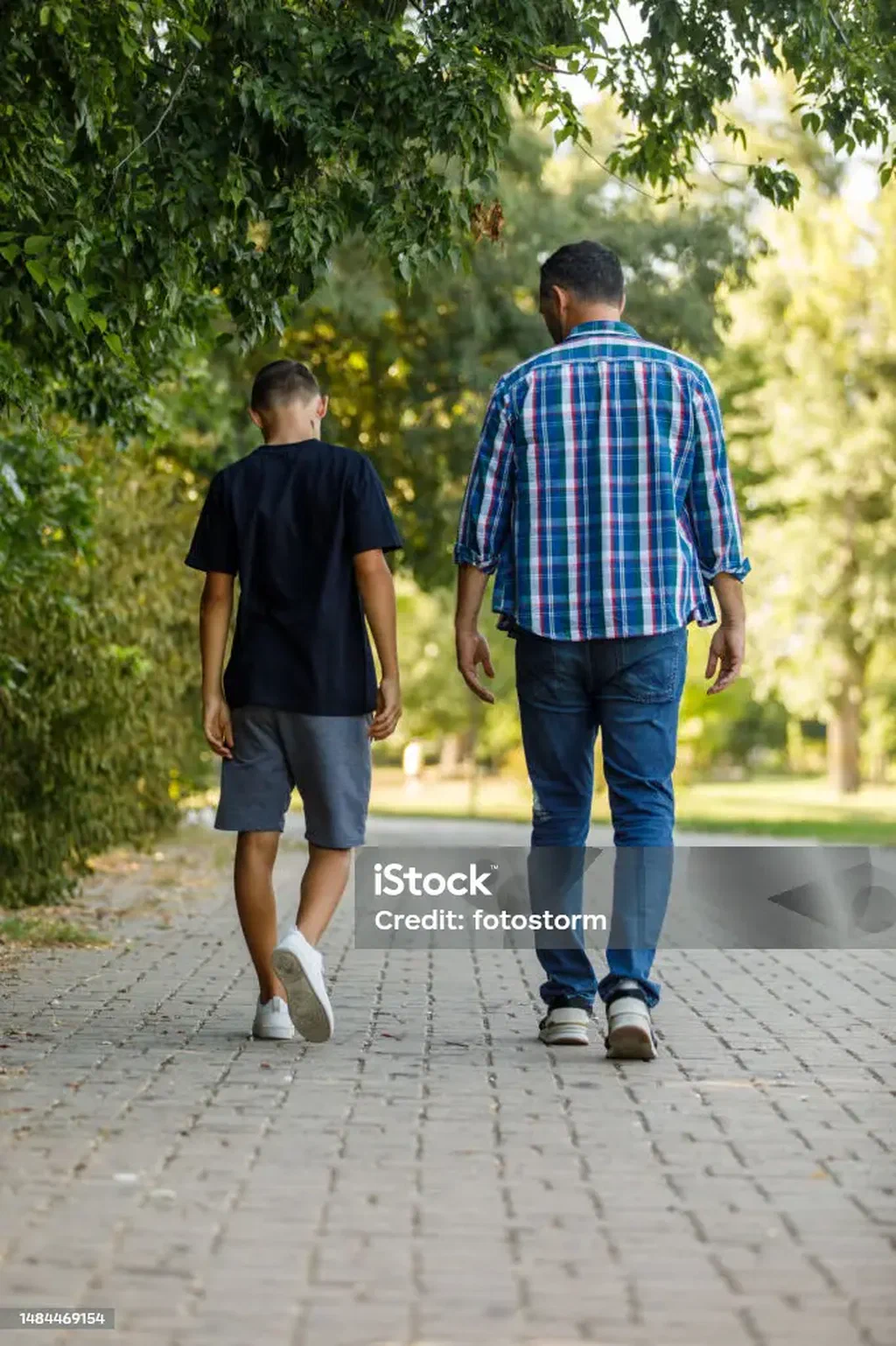 A teenage boy and his father walking in a park at sunset